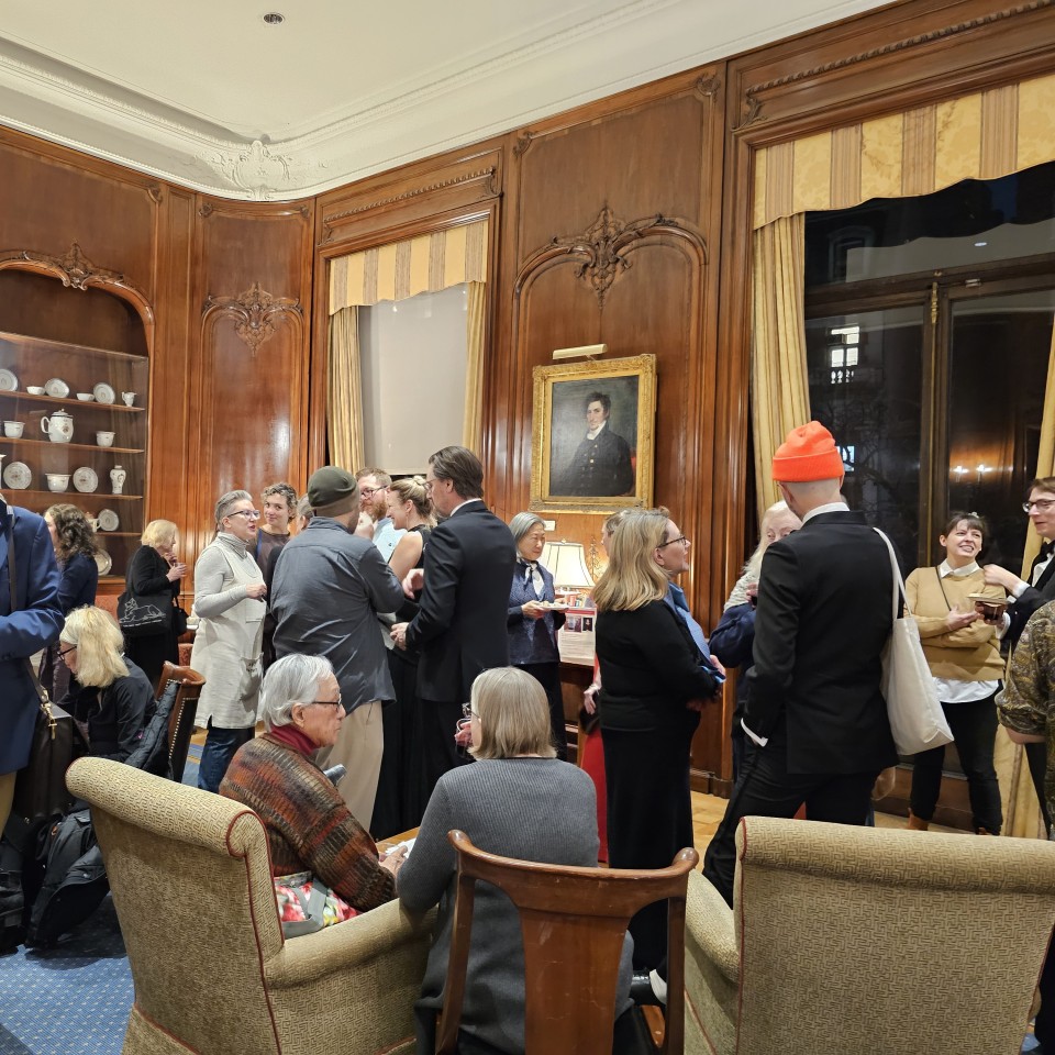 A group of people socializing in an ornately paneled room with a portrait on the wall.